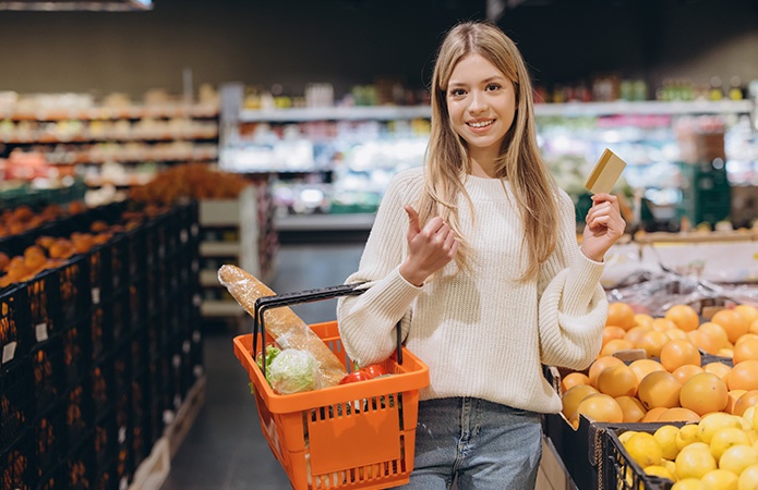 Giovane donna con cestino della spesa e carta di pagamento in un supermercato, simbolo delle scelte dei consumatori influenzate dalle analisi sensoriali alimentari in ambito Food