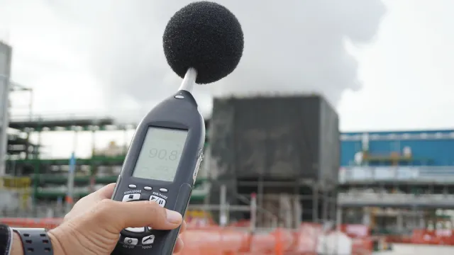 Operatore che tiene in mano un microfono che ha l’obiettivo di misurare l’impatto acustico di un impianto di produzione.