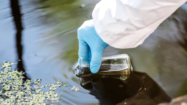 Campionatore dotato di protezioni intento a raccogliere un campione di acqua in un sito contaminato. 