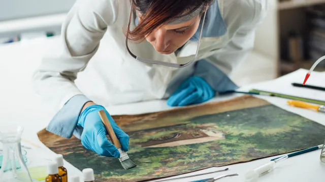 Restauratrice china su una tela mentre con un pennello opera per ripristinare un bene culturale