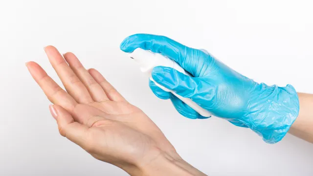 Operatore con guanto intento a spruzzare uno spray disinfettante su una mano per effettuare un test dedicato a biocidi e PMC