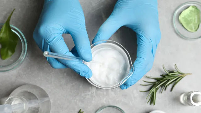 Operatore di laboratorio intento a mescolare un campione cosmetico dal becker, in background dei “raw material”, ingredienti per formulazioni.